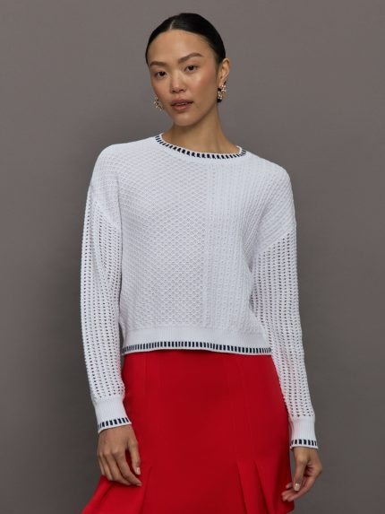 Model wears a lightweight, open knit, drop shoulder sweater with navy trim.