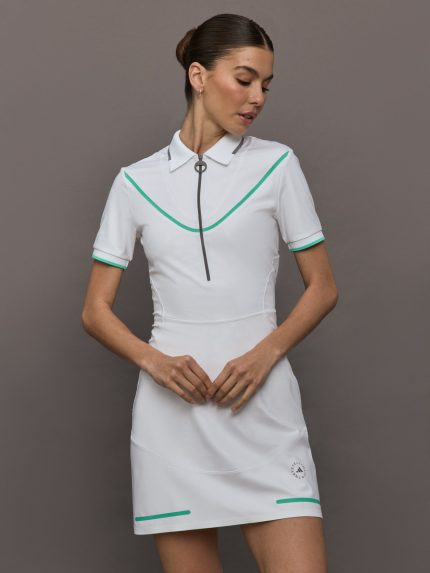 Model wears a fitted collared white short sleeve golf dress with green seams and detailing. 