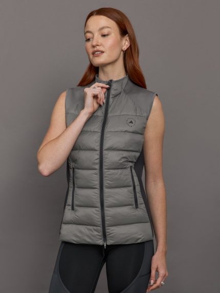 Model wears sleeveless grey golf vest with a high collar, front zipper, and side zip pockets.
