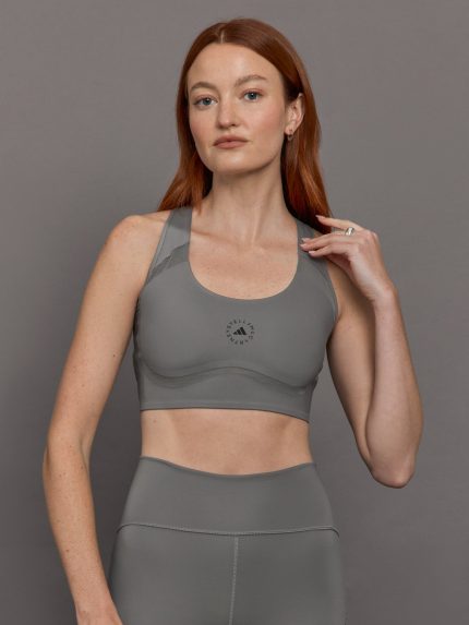 Model wears grey sports bra with a racerback design, mesh panels, and small laser-cut holes.
