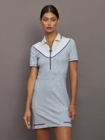 Woman wearing a light blue dress with white collar and purple accents against a gray background