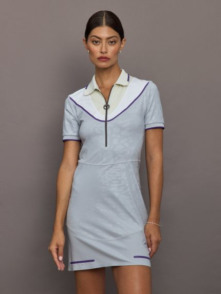 Woman wearing a light blue dress with white collar and purple accents against a gray background