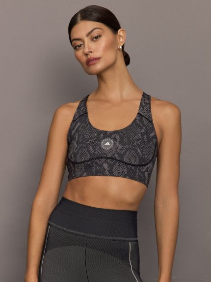 Model wears black/charcoal Adidas sports bra with logo in the center.