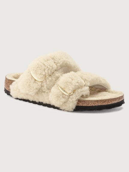 A pair of beige teddy shearling slippers with two adjustable straps and metal pin buckles, featuring an anatomical cork-latex footbed and a platform sole.