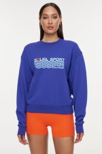 Model wears a royal blue crewneck sweatshirt with the lettering "Soleil Sport" across the chest with wavey lines below and "Bandier" in the bottom right corner.