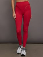 Model wears a sleek, high waisted bright red legging with shiny contoured hip detailing lines.
