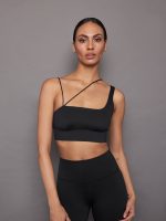 Model wears an asymmetrical strappy sports bra in black.
