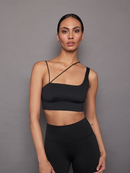 Model wears an asymmetrical strappy sports bra in black.