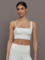 Model wears a white sports bra with one thick strap and two asymmetrical spaghetti straps.
