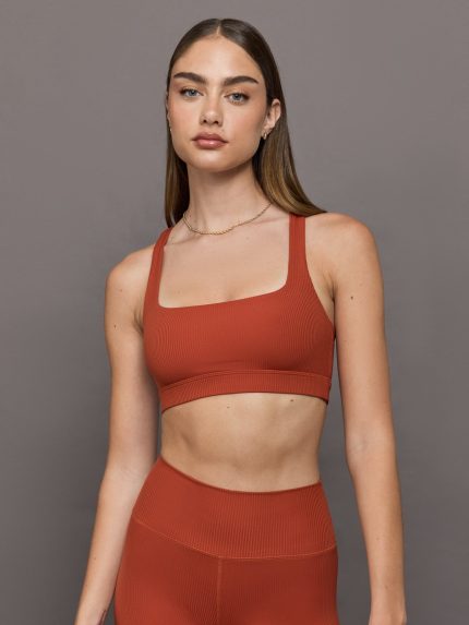 Model wears terracotta-colored racerback bra with a ribbed texture, square neckline, and wide straps that merge at the back.