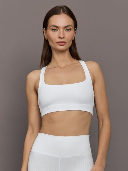 Model wears ribbed, white racerback sports bra with a fitted design and square neckline.