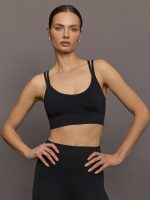 Model wears black sports bra with double thin back straps and a smooth, supportive finish.