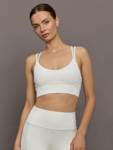 Model wears white active bra with double thin back straps and a smooth, supportive finish.