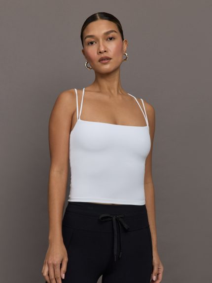 Model wears fitted white tank top with double, thin, adjustable straps and a scoop neckline.