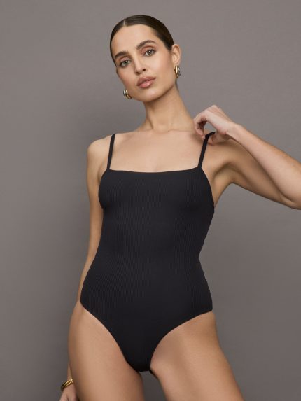 Model wears a black bodysuit with a straight neckline across the chest and thin straps.