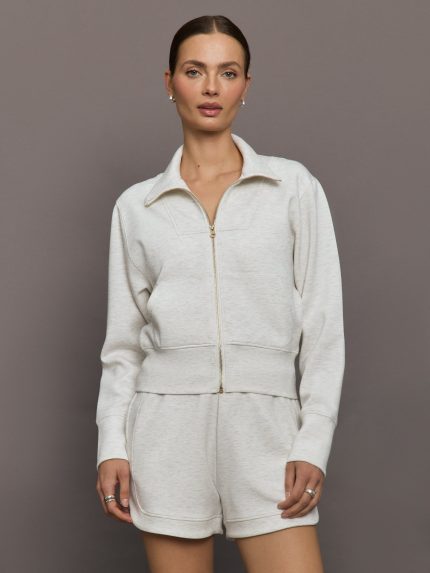Model wears ivory Interlock Full Zip Jacket featuring a sleek, minimalist design with a high collar and full-length zipper.