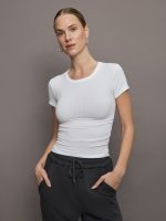 Model wears a short sleeved, ribbed jersey fitted white top with ruching down both sides.