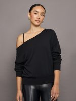 Model wears a black, slouchy French terry sweatshirt with an off-the-shoulder, raw-edged asymmetrical neckline and a relaxed, roomy fit.