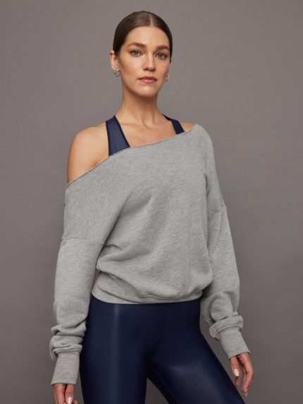 Model wears a grey, slouchy French terry sweatshirt with an off-the-shoulder, raw-edged asymmetrical neckline and a loose, relaxed fit.     