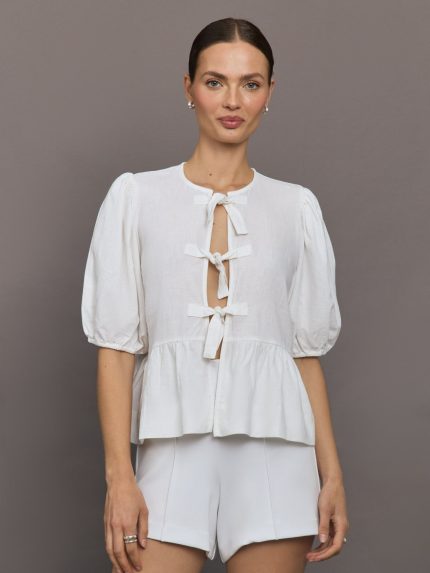 Model wears white puff sleeve top with a front ties and high neckline.