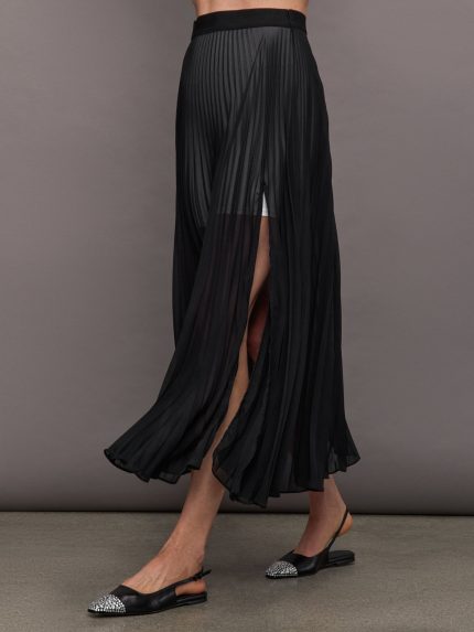 A model wears a black, long, sheer mesh pleated skirt with an elastic waistband and a slit on one side.