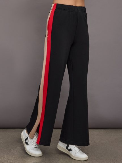 Model wearing black wide-leg track pants with a red and beige stripe on the side.