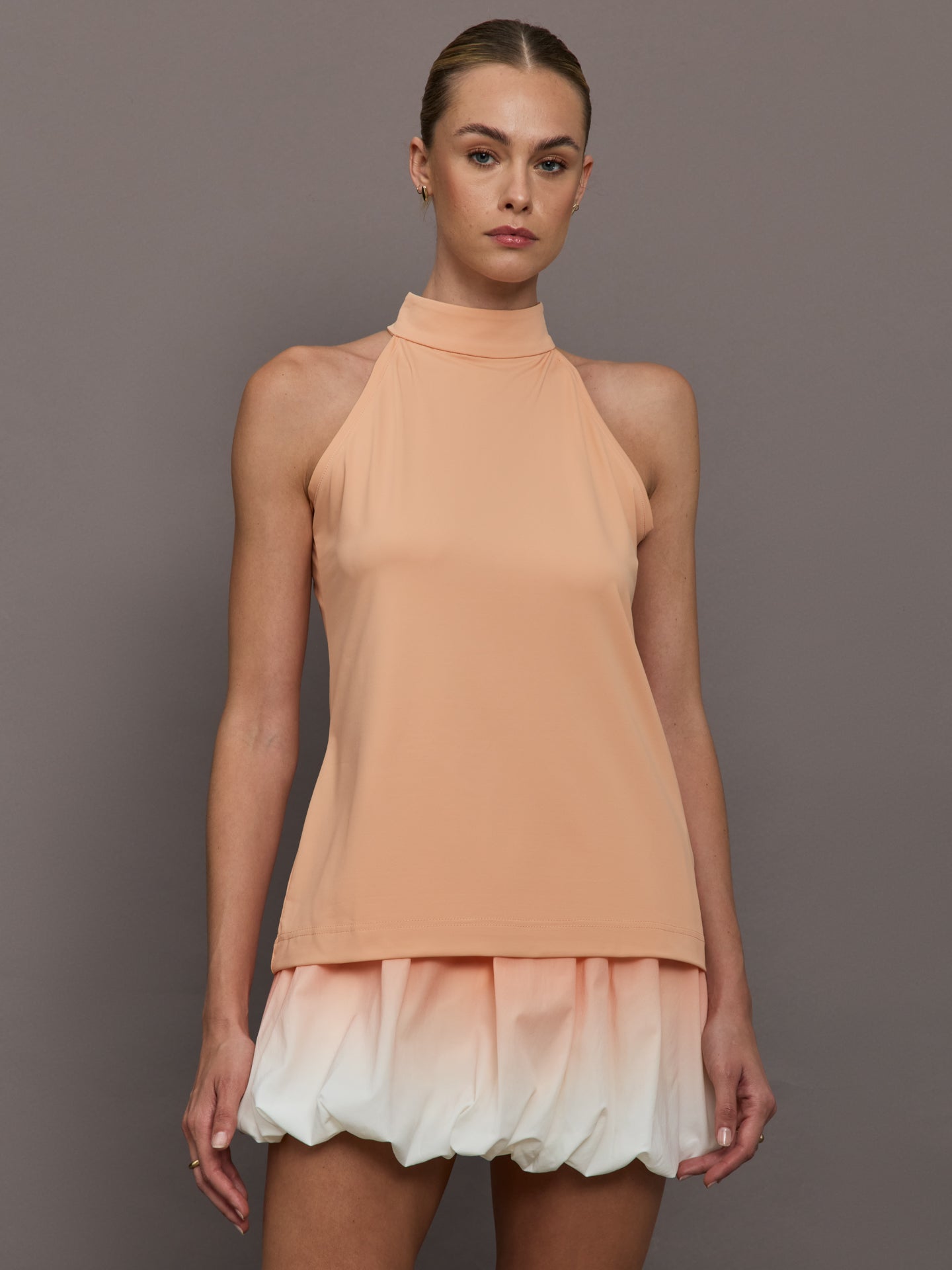 EUGE-31214-35225-PNKPINLT-Sofia-color-Peach_41133-Edit Model is wearing a peach mock neck halter top and skirt against a plain background.