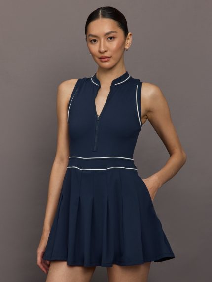Model wears a navy sleeveless activewear dress with white piping. 