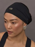 Model wears a black headwrap with small gold goldbergh logo above forehead.