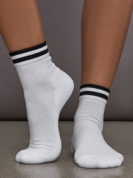 Model wears white athletic sock with contrast stripe patterning.
