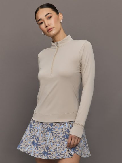 Woman wearing a beige long-sleeve top and floral skirt against a gray background
