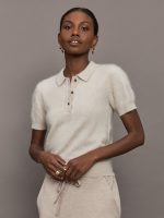Model wears a neutral colored button up short sleeved polo sweater in a wool/cashmere blend.