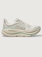 Chunky soled white Hoka running shoe with pastel green trim.