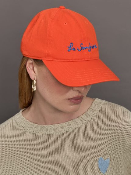 Model wears an orange baseball cap with blue script lettering "Le Sunshine" across front.