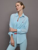 Model wears light blue button down shirt with tiny red heart over left side of chest.
