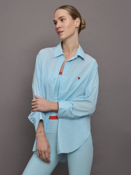 Model wears light blue button down shirt with tiny red heart over left side of chest.