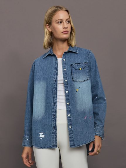 Woman wearing a blue denim jacket over a white outfit on a gray background