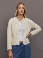 Woman wearing a beige textured cardigan over a white top and blue pants on a gray background