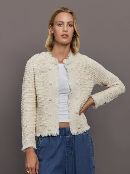Woman wearing a beige textured cardigan over a white top and blue pants on a gray background