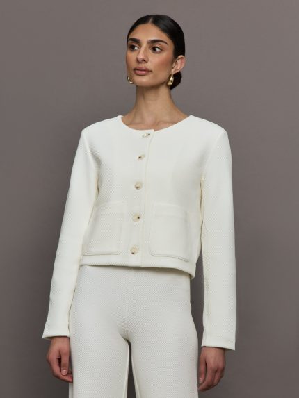 Model wears a button down boxy white boatneck sweater with symmetrical front pockets above the waist. 