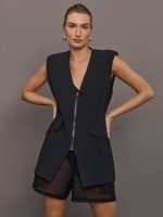 Model wears black Odyssey Vest with a boxy silhouette and silver front zip and v-neckline.