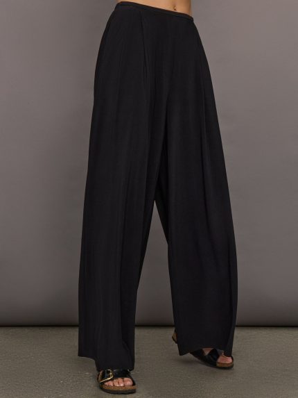 Model wears a pair of mid rise black pleated wide leg dress pants.