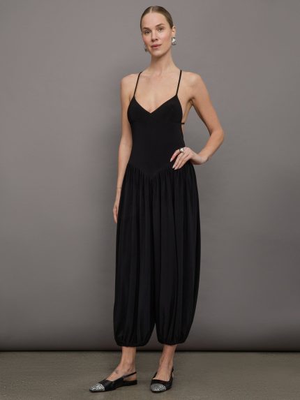 Model wears a v neck, drop waist black jumpsuit with pleated balloon cropped legs.