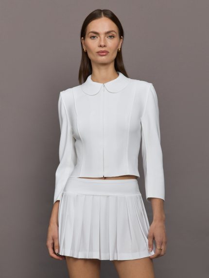 Model wears white jacket with a front zipper, collared neck and long sleeves.     