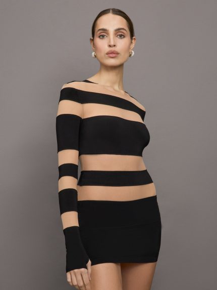Model wears a long sleeved minidress with thick alternating stripes of black and sheer/mesh. 