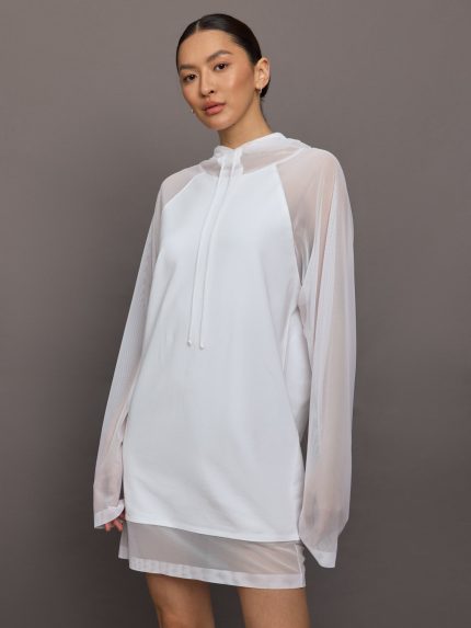 Model wears the Oversized Snow White mini dress featuring raglan sleeves, a hood, and mesh panel detailing.
