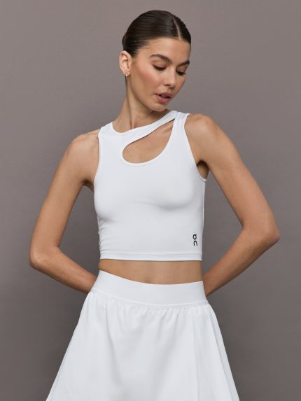 Model wears an asymmetric cut out cropped active tennis tank top in white.