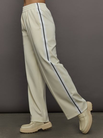 Model wears an off white track pant with blue seamed detailing down the sides. 