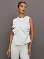 Model wears a sleeveless white top with ruffles.