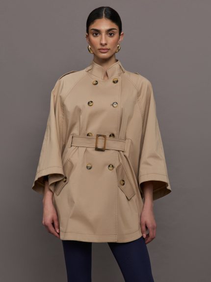 Model wears a tan high neck bell sleeved trench with double breasted buttons and a belted high waist.